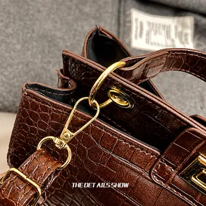 Détail du sac en cuir marron foncé texture crocodile avec crochet en métal doré brillant
