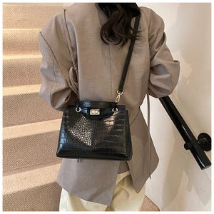 Detail van zwarte handtas met krokodillentextuur en gouden gesp gedragen door model