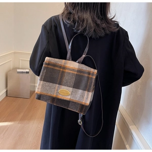 Détail d'un sac à dos en laine à carreaux avec lanières cuir et logo en métal doré