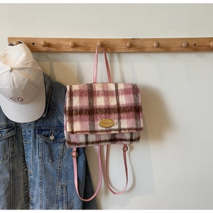 Détail d'un sac à dos en peluche à carreaux roses avec plaque logo dorée et chaînes