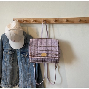 Détail d'un sac à dos en laine à carreaux violets avec emblème doré et texture pelucheuse