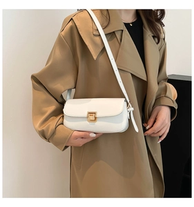 Sac à bandoulière en cuir blanc avec boucle dorée porté sur un manteau beige