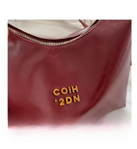 Macro shot of dark red crescent bag featuring glossy texture and golden metal logo