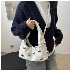 Détail d'un sac bandoulière blanc en cuir avec gros clous argentés porté par un modèle