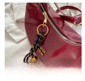 Detail of glossy dark red crescent bag featuring gold zipper and unique woven charm
