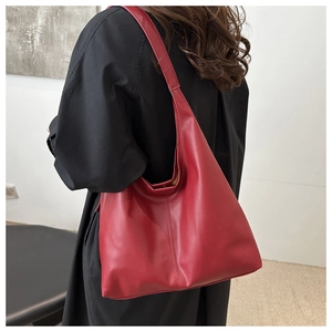 Close-up of a burgundy leather tote bag with vertical stitching on a model in a black coat