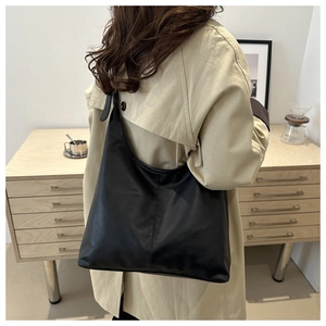 Detail of minimalist black matte leather tote bag worn with beige trench coat