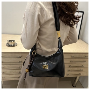 Detail of glossy black crescent bag featuring woven rope charm and golden hardware