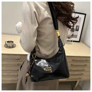 Detail of black glossy leather crescent bag with gold logo and woven charm accessory