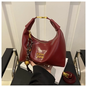 Detail of burgundy crescent shoulder bag featuring gold hardware and logo branding