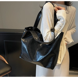 Detail of the glossy wrinkled leather texture and wide shoulder strap on a black tote bag