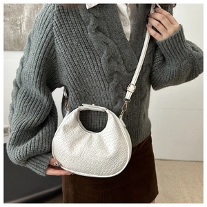 Gros plan d'un sac demi-lune blanc tressé avec boucle dorée porté par un mannequin