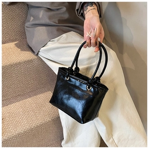 Detail of a black glossy leather handbag with silver eyelets and sturdy double handles