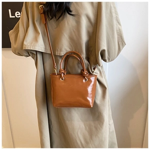 Detail of a brown glossy leather bucket bag with knotted handle on a trench coat model