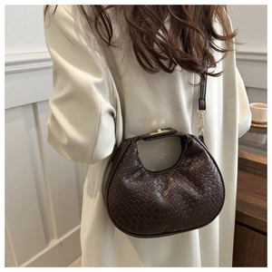 Détail du sac demi-lune tressé marron foncé avec boucle dorée sur manteau