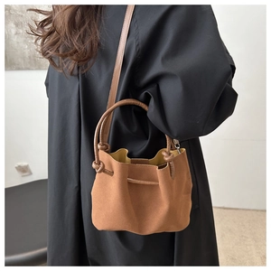 Brown suede bucket bag with unique knotted handle styled on a black winter wool coat