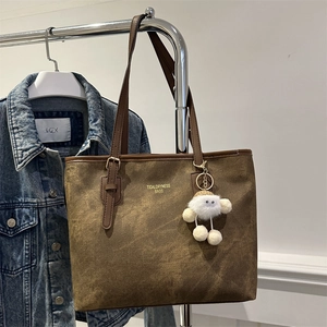 Brown suede tote bag with leather handles and plush charm hanging on a hanger