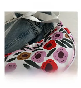 Close-up of a floral crescent crossbody bag with white fabric strap on denim fabric