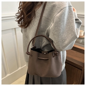 Detail of dark brown drawstring bucket bag featuring matte leather and a knot design