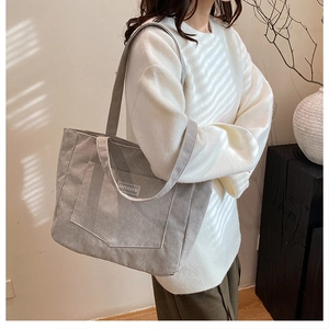 Detail of light grey corduroy tote bag featuring front pocket and embroidered text
