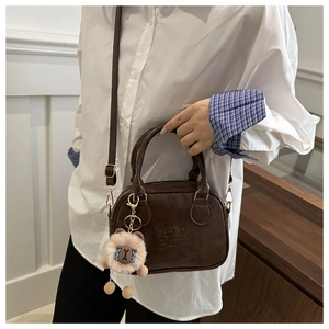 Detail of dark brown leather square bag with lion charm and adjustable shoulder strap
