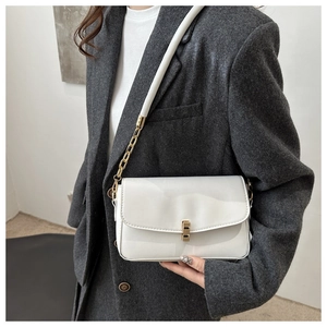 Detail der weißen Lackleder-Schultertasche mit Goldschließe und Kettenriemen am Modell