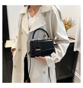 Detail of glossy black patent leather handbag featuring a large buckle and slim strap