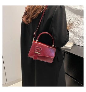 Detail of burgundy glossy leather crossbody bag with square buckle on a model