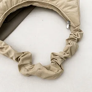 Detalle del bolso beige con correas fruncidas suaves y cierre de cremallera metálica