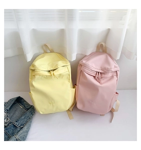 Detalle de mochilas de nailon en amarillo y rosa con logo frontal y tiradores de nudo