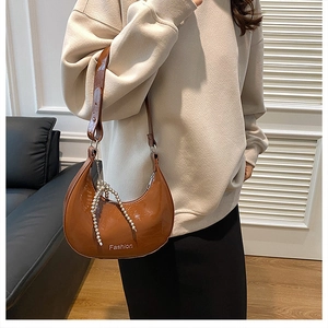 Brown semi-circle shoulder bag with pearl tassel and smooth glossy finish on model