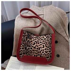Detail of leopard print canvas bag with red leather trim on beige coat background