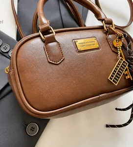 Detail der braunen Vintage-Bowlingtasche mit goldenem Abakus-Anhänger und Namensschild