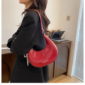 Red crescent shoulder bag with glossy leather finish and heart charm on black blazer