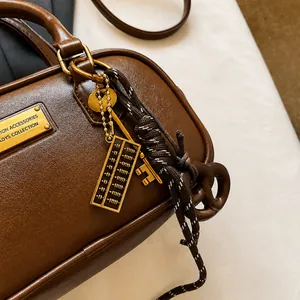 Detail einer dunkelbraunen Ledertasche mit Goldplakette und Miniatur-Abakus-Anhänger