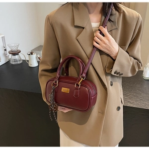 Details der burgunderroten Bowlingtasche mit goldener Plakette und dekorativem Seidenschal