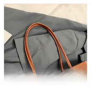 Detailed view of brown leather bag with slim dual handles and decorative red tassel