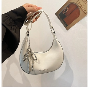 Close-up of a white leather crescent bag with silver beads bow charm and Fashion print