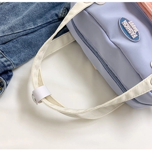 Dettaglio della borsa a tracolla in nylon lilla con stemma blu 'FASHION Happy' e fibbia