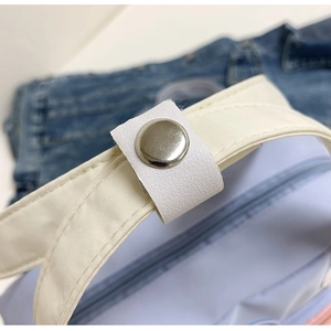 Dettaglio del bottone a pressione argento e cinturino in pelle sintetica su borsa blu