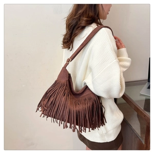 Detail of a brown suede shoulder bag featuring long fringe and a minimalist bohemian aesthetic
