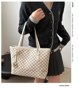 Close-up of beige tote bag featuring repetitive M-letter print and round metal logo charm