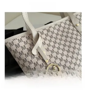 Close-up of beige monogram tote bag featuring gold metal pendant and textured leather
