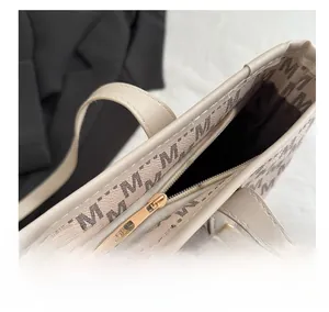 Macro shot of smooth gold metal zipper and letter M print on beige tote bag texture