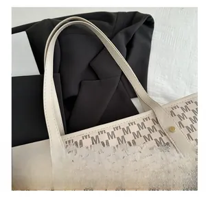 Detail of white tote bag featuring M-pattern print and leather handle with gold rivets