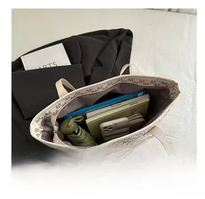 Spacious interior of beige tote bag with M-print showing items like books and umbrella