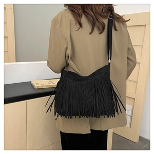 Detail view of a black faux suede tote bag featuring long fringes and adjustable strap
