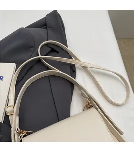 Detail van een crème schoudertas met gouden gesp en verstelbare riem op een blazer