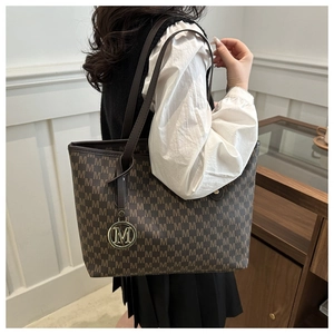 Detail of the large tote bag showing 'M' letter print and a metallic logo charm