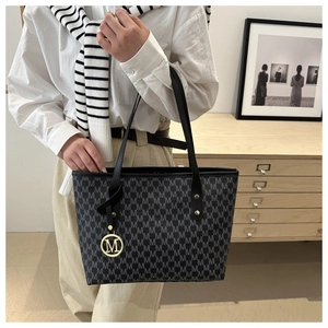 Close-up of tote bag featuring all-over M pattern and golden metal logo pendant